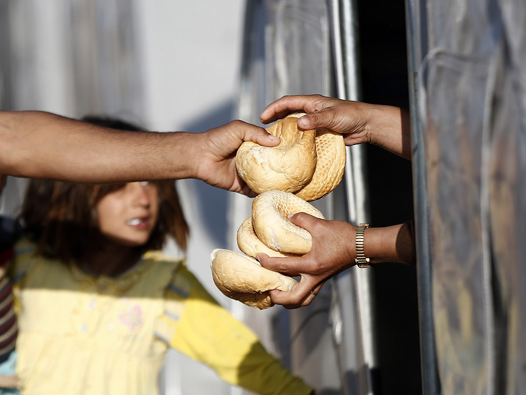 Кюрд доброволец дава хляб на сирийска жена в бежански лагер в района Шанлъурфа, Турция