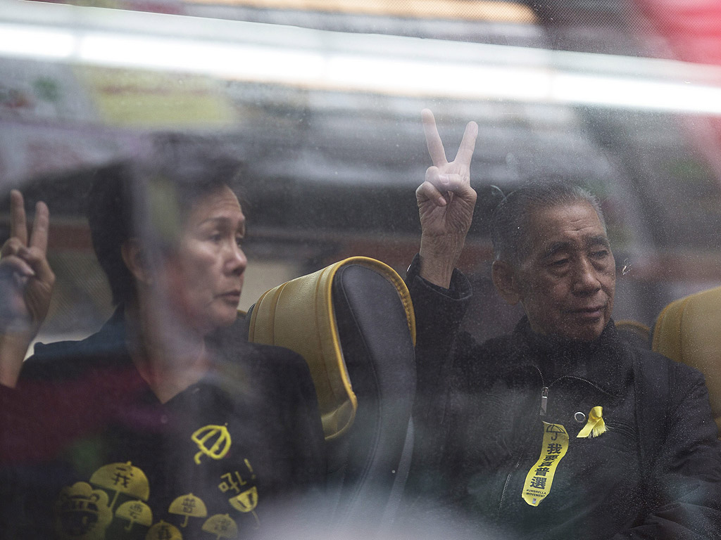15 декември. Демонстранти показват знака на победата през прозореца на полицейски автобус, след като бяха задържани от полицията прочистваща лагерите на протестиращите в Хонконг.