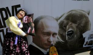 Севернокорейска туристка позира със сувенирна възглавница с лика на Ким Чен-ун пред плакат, изобразяващ Владимир Путин и мечка в Парка на победата в Москва