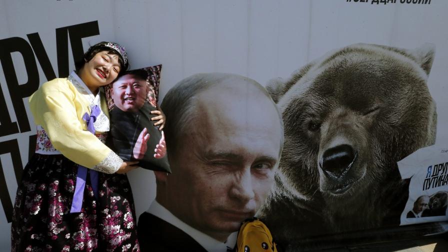 Севернокорейска туристка позира със сувенирна възглавница с лика на Ким Чен-ун пред плакат, изобразяващ Владимир Путин и мечка в Парка на победата в Москва