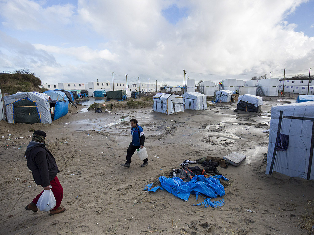 Мигранти сред палатките и бараките на импровизирания лагер, наречен Джунглата до нов лагер от контейнери, подготвени да се използват като жилища в Кале, Франция. Имигрантите, опитващи се дастигнат до Великобритания са между 4000 и 7000 в Кале