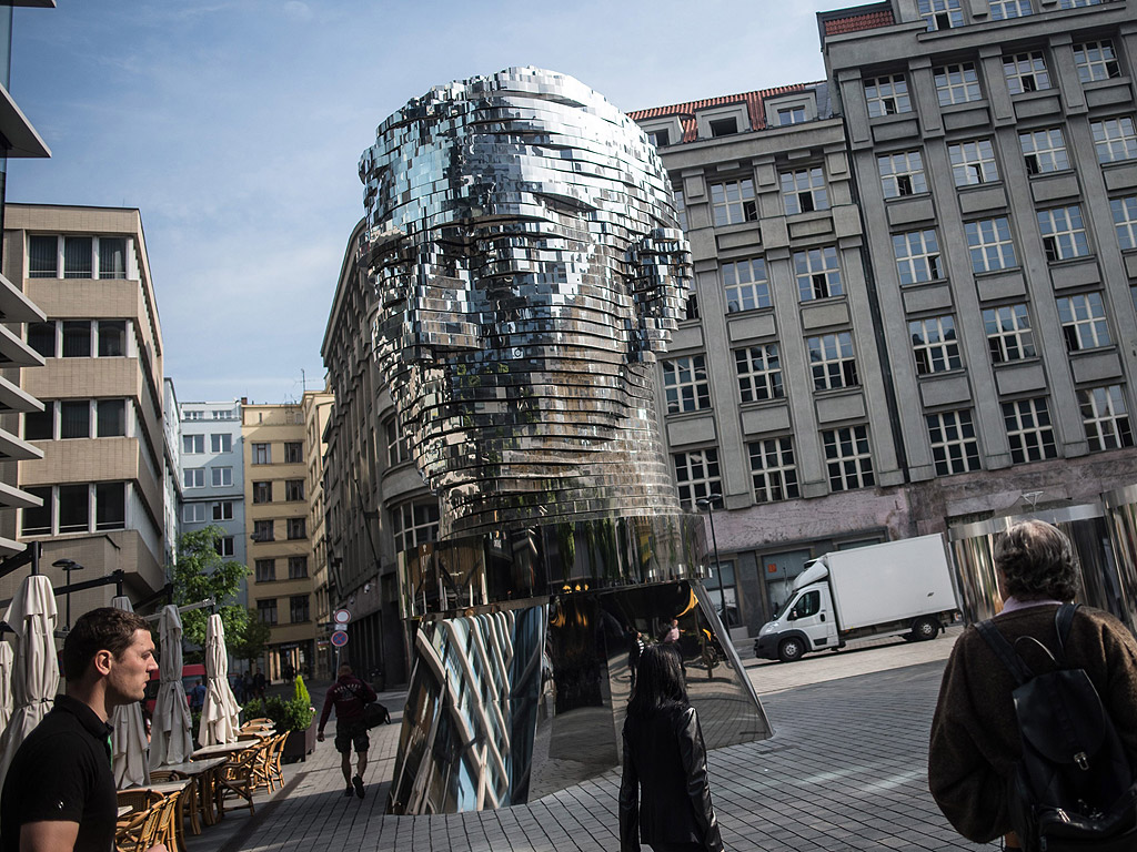 Пешеходци до статуя на гигантска въртяща се глава на писателя Франц Кафка в центъра на Прага, Чехия. Статуята на родения в Прага (тогава част от Австро-Унгария), известен писател Кафка е изработена от чешкия художник Черни