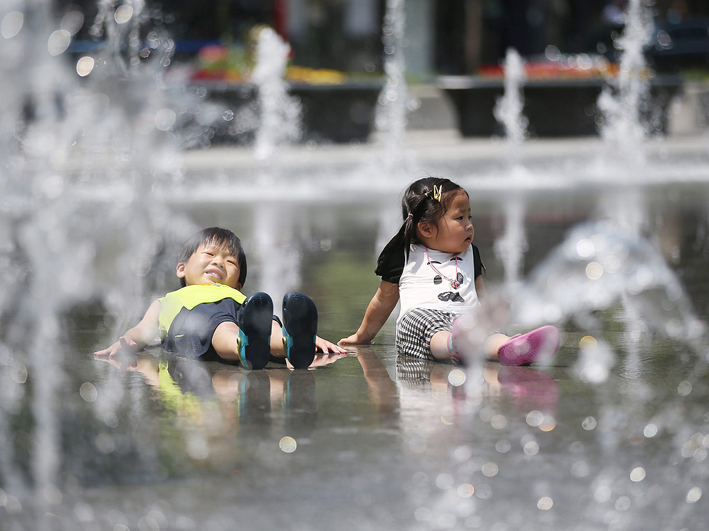 Две деца в средата на мини-фонтани в центъра на Сеул, Южна Корея през горещ ден