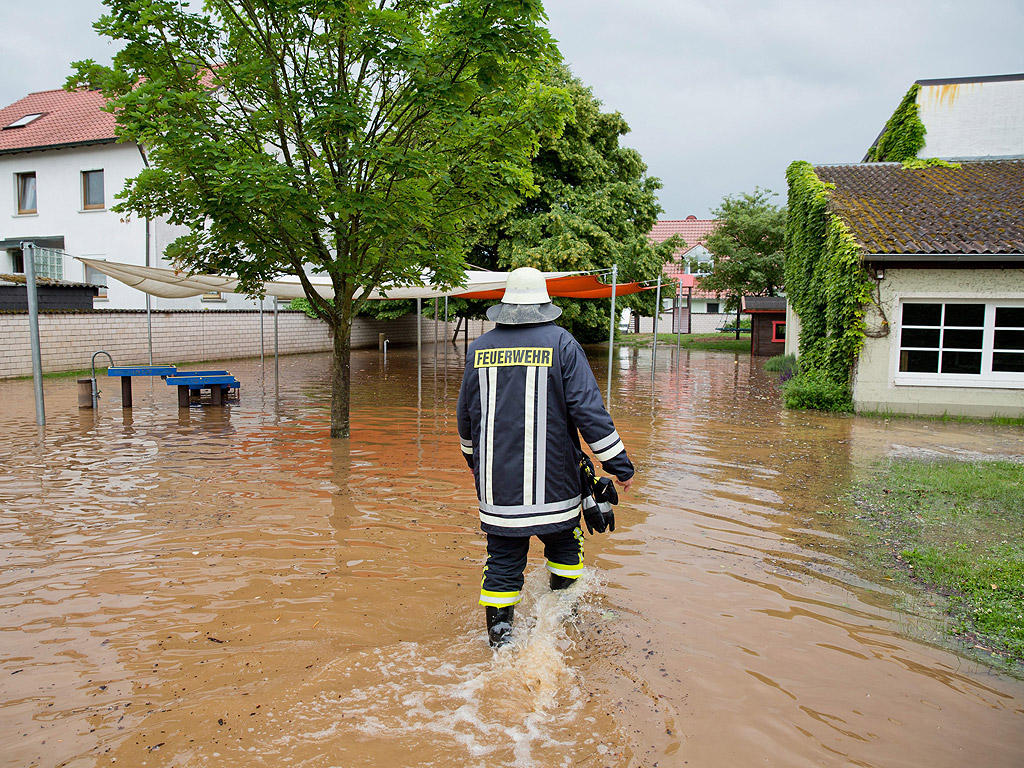 Пожарникар ходи през наводнена детската площадка в Оберхайд, Германия, след пороен дъжд