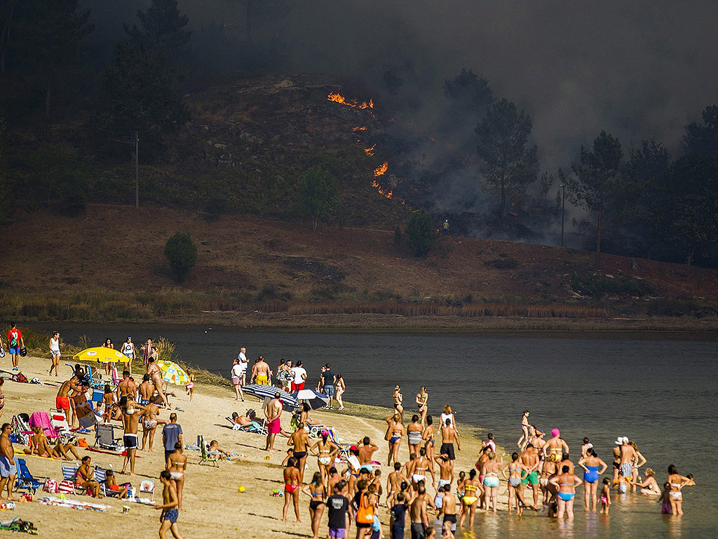 Почиващи гледат от плажа на река Вердуго пожар, който започна в село Сотомайор в Понтеведра, северозападна Испания и достигна до границата на Испания с Португалия