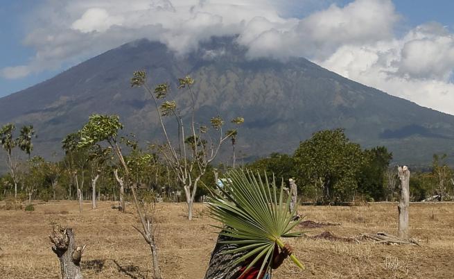 Жена върви на фона на вулкана Агунг на о-в Бали