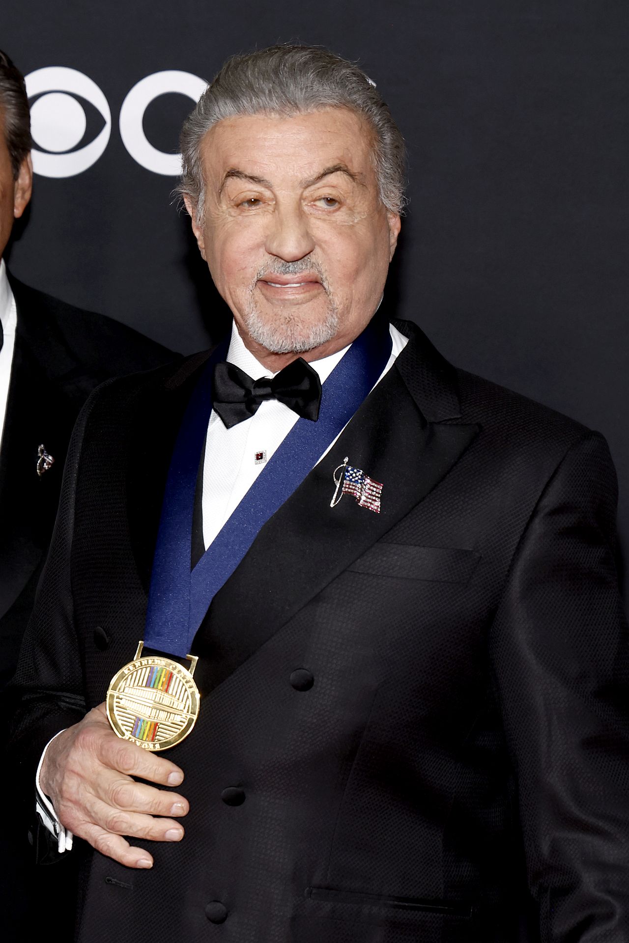 Легендата от „Роки“, на 79 години, се подпираше на елегантен черен бастун със златиста дръжка, докато правеше внушително влизане в Kennedy Center Opera House в събота вечер, където беше почетен като един от тазгодишните носители на отличието. ъпреки новата си опора на бастуна, Сталоун се усмихваше, разговаряше с други отличени и изглеждаше готов да се наслади на вечерта – макар че бавната и внимателна походка рязко контрастираше с безстрашния екшън герой.