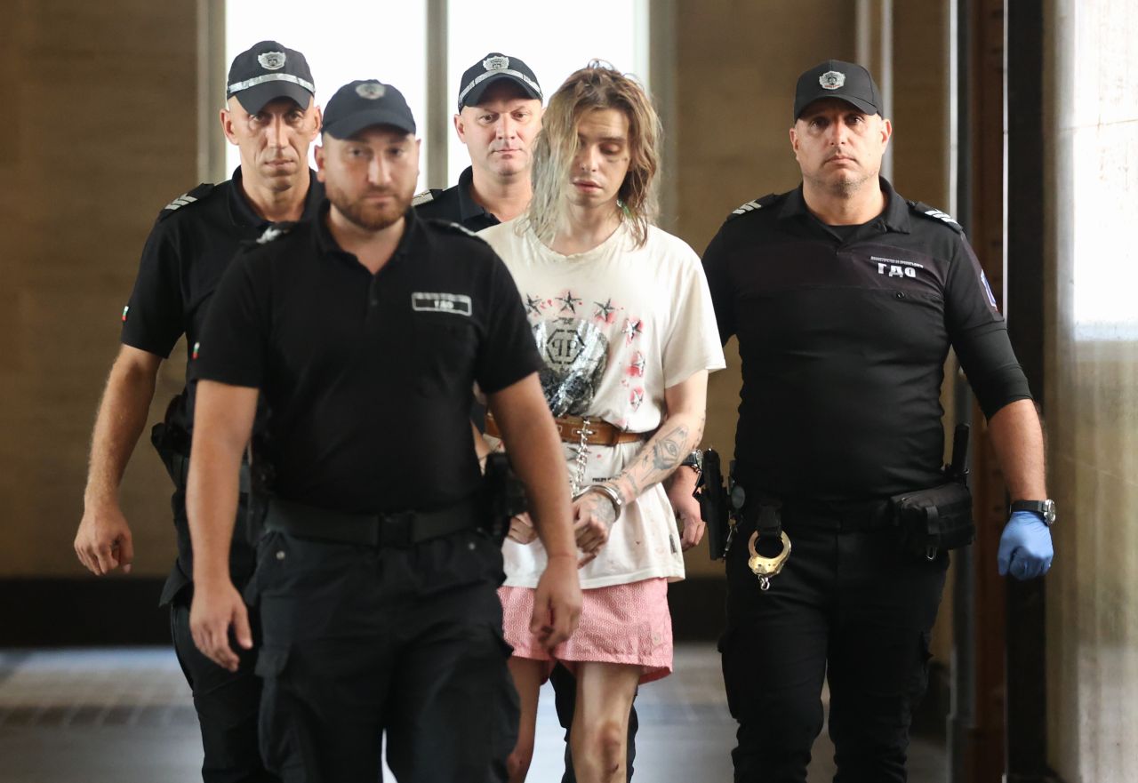 <p>Окован в белезници и пранги на краката, украинецът Ярослав Гуляткин бе доведен под засилен конвой в Съдебната палата. Задържаният за убийство на жена в София направи впечатление с татуировките по лицето и нетипичното си облекло по време на делото за мярката му.</p>