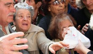 Възрастни хора протягат ръце към пакети с помощи, раздавани от Червения кръст