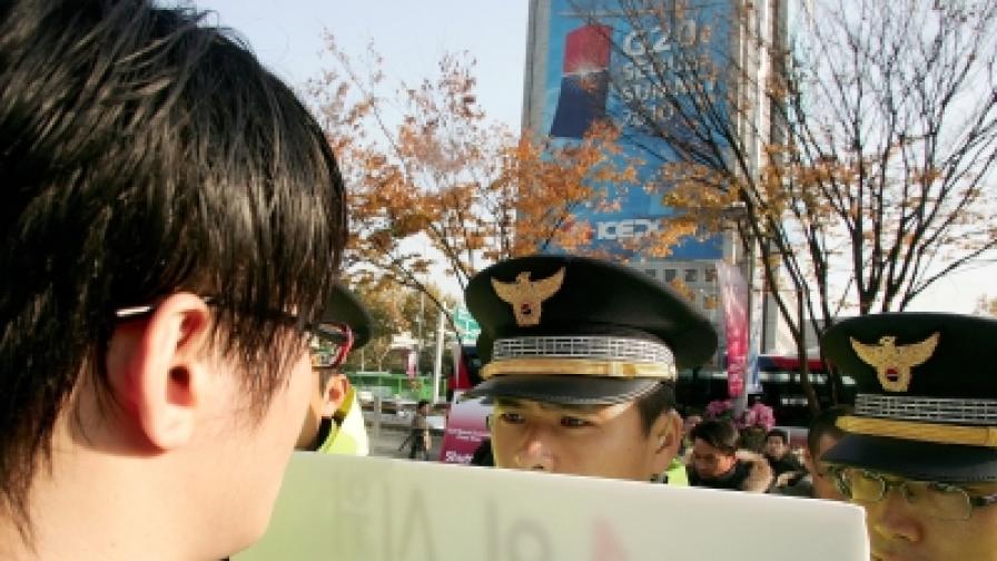Полицаи спират протестиращ, който им показва лозунг срещу срещата на Г-20 в центъра на Сеул