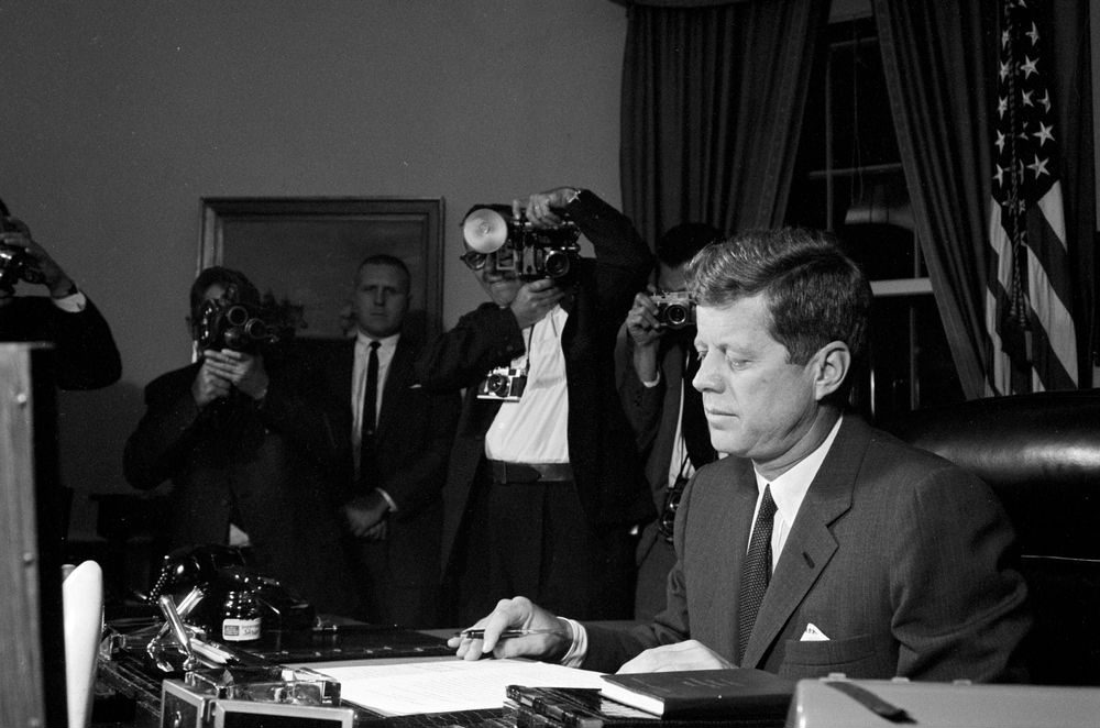 На 22 ноември 1963 г. президентът на САЩ Джон Ф. Кенеди е смъртоносно прострелян, докато кортежът му минава по "Дийли плаза" в Далас, щата Тексас. 

За убийството му е обвинен Лий Харви Осуалд. Два дни след убийството на Кенеди обаче е застрелян и самият Осуалд. 

Убиецът му - Джак Руби, е осъден на смърт. Руби обжалва наказанието си, но докато чака ново разглеждане на делото, се разболява от рак на белите дробове. Умира в затвора на 3 януари 1967 г.