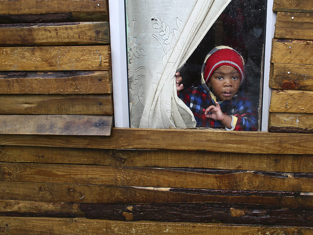 Дете гледа през прозореца на барака в наводненото селище Масифумелеле в покрайнините на Кейп Таун, РЮА, на 15 август. Над 3500 души са били принудени да напуснат подобни примитивни жилища заради поройни дъждове и наводнения в Кейп Таун това лято.